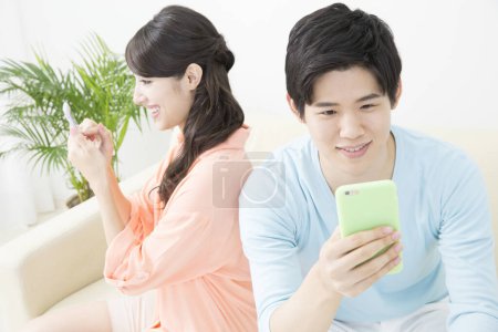 Téléchargez les photos : Jeune couple asiatique à l'aide de smartphones dans le salon - en image libre de droit