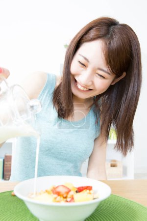 Photo for Smiling asian female eating healthy breakfast - Royalty Free Image