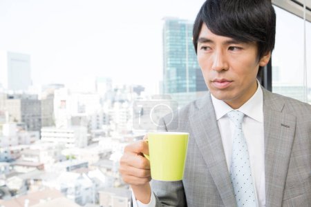 Téléchargez les photos : Asiatique homme d'affaires boire du café dans le bureau - en image libre de droit