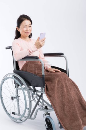 Téléchargez les photos : Femme en fauteuil roulant en utilisant smartphone sur fond isolé - en image libre de droit