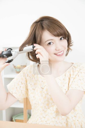Photo for Young asian woman with  curling iron sryling her hair - Royalty Free Image