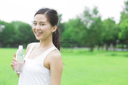Foto de Hermosa mujer japonesa bebiendo agua en el verde parque de verano durante el día - Imagen libre de derechos
