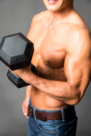 Foto de Joven musculoso hombre en gimnasio con mancuerna - Imagen libre de derechos