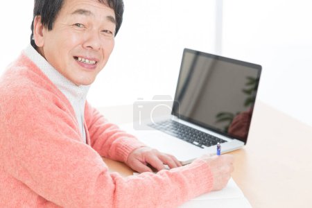 Téléchargez les photos : Homme âgé souriant utilisant un ordinateur portable à la maison. - en image libre de droit