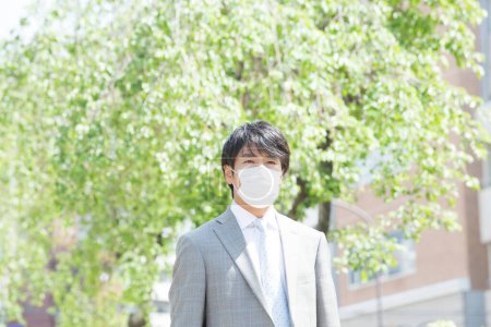 Téléchargez les photos : Beau professionnel japonais homme d'affaires en masque visage sur la rue - en image libre de droit