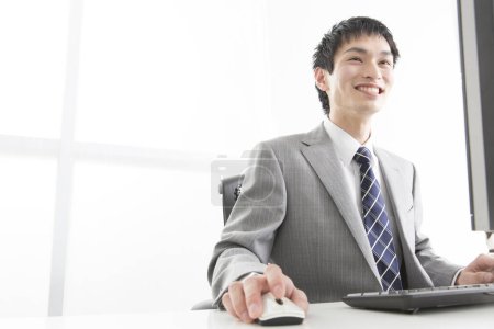Téléchargez les photos : Portrait en gros plan d'un jeune homme d'affaires japonais travaillant avec un ordinateur au bureau - en image libre de droit
