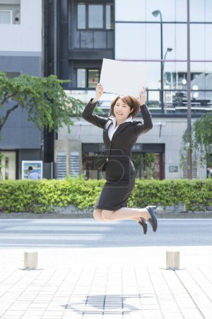 Téléchargez les photos : Portrait d'une jeune femme d'affaires avec une pancarte vierge sautant en ville - en image libre de droit