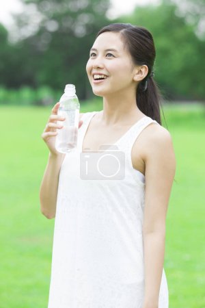 Foto de Hermosa mujer japonesa bebiendo agua en el verde parque de verano durante el día - Imagen libre de derechos