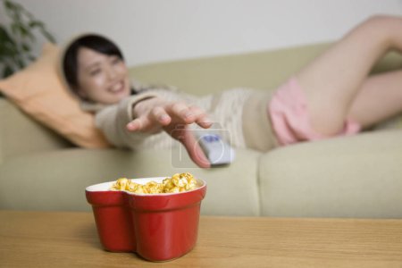 Téléchargez les photos : Asiatique jeune femme manger popcorn tout en regardant la télévision - en image libre de droit