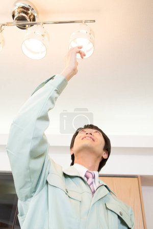 Téléchargez les photos : Asiatique mâle électricien changer ampoule - en image libre de droit
