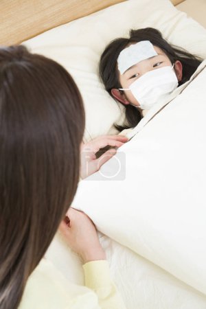 Téléchargez les photos : Asiatique femme avec une malade fille couché sur l 'lit - en image libre de droit
