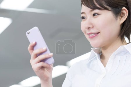 Téléchargez les photos : Femme tenant un téléphone portable au bureau - en image libre de droit