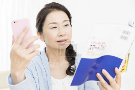 Photo for Asian young woman reading a book while reading a message - Royalty Free Image