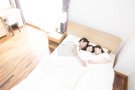 Téléchargez les photos : Asiatique mignon trois membres famille, père, mère, petite fille, dormir dans la chambre à coucher dans un lit confortable ensemble - en image libre de droit