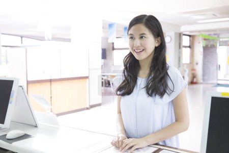Photo for Young Japanese woman standing at reception desk at driving school - Royalty Free Image