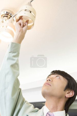 Photo for Asian male electrician changing  light bulb - Royalty Free Image
