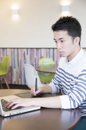 Téléchargez les photos : Jeune Japonais travaillant sur ordinateur portable. Graphiste au travail - en image libre de droit