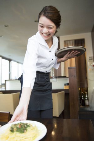 Photo for Smiling asian waitress serving dish - Royalty Free Image