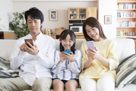 Téléchargez les photos : Famille heureuse avec smartphones sur canapé à la maison - en image libre de droit
