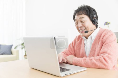 Téléchargez les photos : Asiatique homme dans un casque et avec ordinateur portable de travail à la maison - en image libre de droit