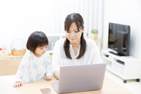 Téléchargez les photos : Jeune mère et petite fille utilisant un ordinateur portable à la maison - en image libre de droit