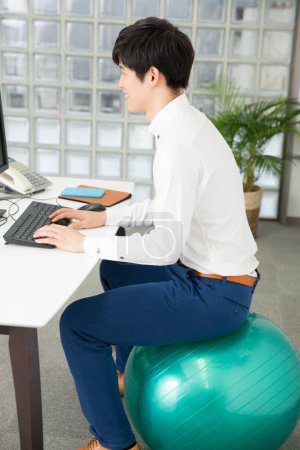 Téléchargez les photos : Homme d'affaires sur ballon en forme de travail sur ordinateur dans le bureau - en image libre de droit