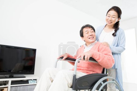 Téléchargez les photos : Jeune asiatique homme en fauteuil roulant regarder la télévision avec son épouse - en image libre de droit