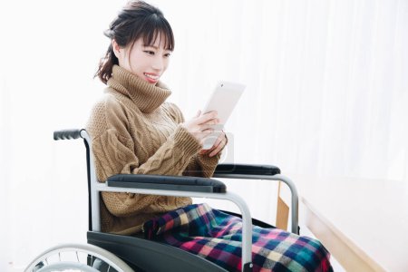 Foto de Mujer asiática en silla de ruedas usando tableta - Imagen libre de derechos