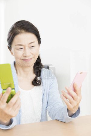 Photo for Close up senior asian woman comparing two phones - Royalty Free Image