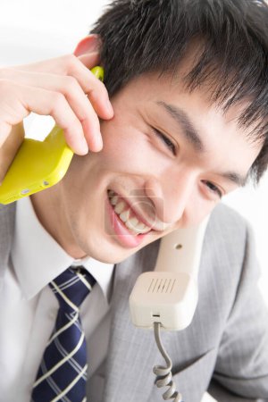 Téléchargez les photos : Portrait en gros plan de jeune homme d'affaires japonais parlant par deux téléphones - en image libre de droit