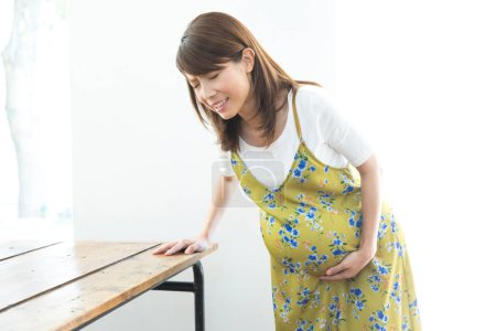 Foto de Asiático embarazada mujer en cocina teniendo estómago dolor. - Imagen libre de derechos