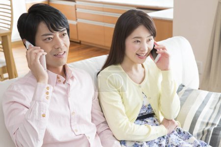 Photo for Asian couple talking on smartphones  at home - Royalty Free Image