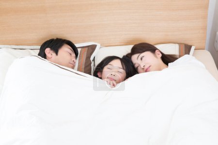 Téléchargez les photos : Asiatique mignon trois membres famille, père, mère, petite fille, dormir dans la chambre à coucher dans un lit confortable ensemble - en image libre de droit