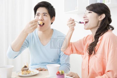 Téléchargez les photos : Asiatique femme manger gâteau avec mari dans salon - en image libre de droit