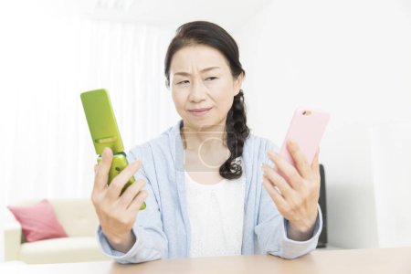 Foto de Primer plano senior asiático mujer comparando dos teléfonos - Imagen libre de derechos