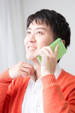 Photo for Young asian man smiling while talking on smartphone - Royalty Free Image