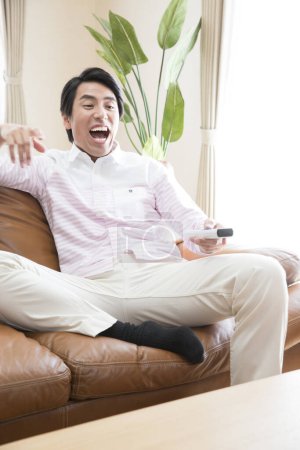 Téléchargez les photos : Asiatique homme regarder tv dans maison salon - en image libre de droit