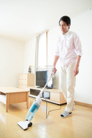 Foto de Asiático hombre limpieza casa con aspiradora - Imagen libre de derechos