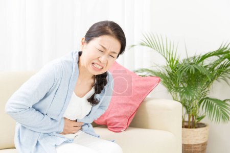 Foto de Mujer asiática teniendo dolor de estómago en sofá - Imagen libre de derechos