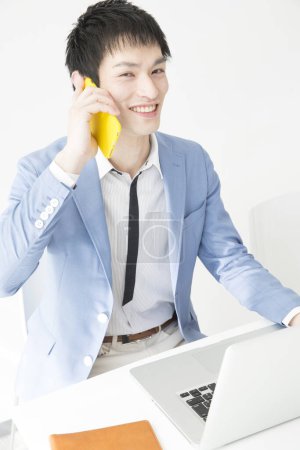 Téléchargez les photos : Portrait en gros plan d'un jeune homme d'affaires japonais parlant par téléphone au bureau - en image libre de droit