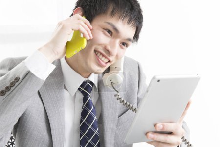 Téléchargez les photos : Portrait en gros plan d'un jeune homme d'affaires japonais parlant par smartphone et utilisant une tablette - en image libre de droit