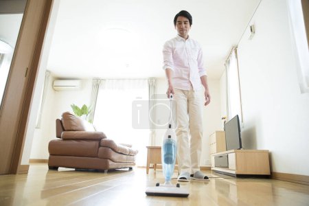 Téléchargez les photos : Jeune asiatique homme nettoyage maison avec aspirateur - en image libre de droit