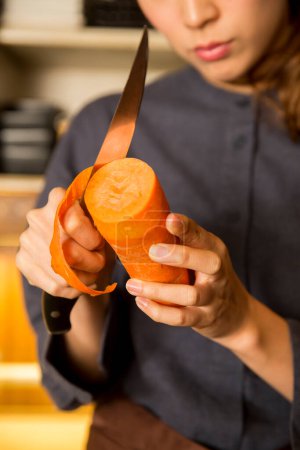 Téléchargez les photos : Jeune asiatique femme serveuse peeling carotte dans cuisine - en image libre de droit