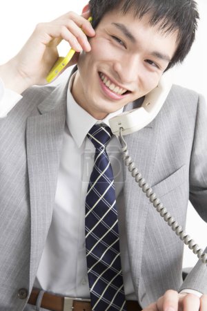 Foto de Primer plano retrato de un joven empresario japonés hablando por dos teléfonos - Imagen libre de derechos