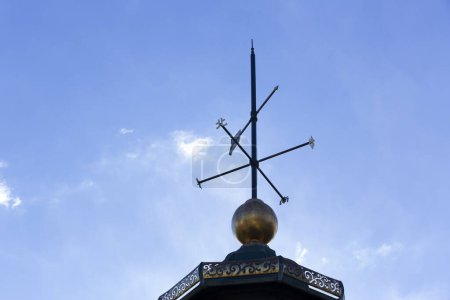 Weather vane placed on a roof, cloudy sky background 