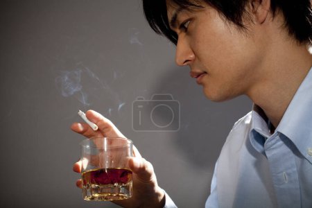 Téléchargez les photos : Asiatique jeune homme fumer cigarette boire whisky - en image libre de droit