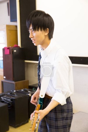 Téléchargez les photos : Japonais écolier jouer de la guitare électrique en classe - en image libre de droit