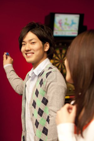 Téléchargez les photos : Jeune couple japonais jouer jeu de fléchettes - en image libre de droit