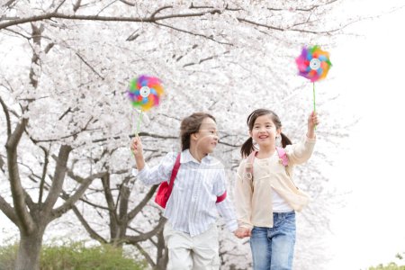 Photo for Happy Japanese schoolchildren with pinwheels in spring park - Royalty Free Image