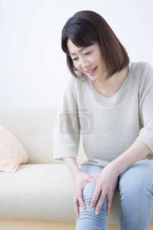 Foto de Retrato de adulto asiático mujer con la pierna dolor en luz casa interior - Imagen libre de derechos